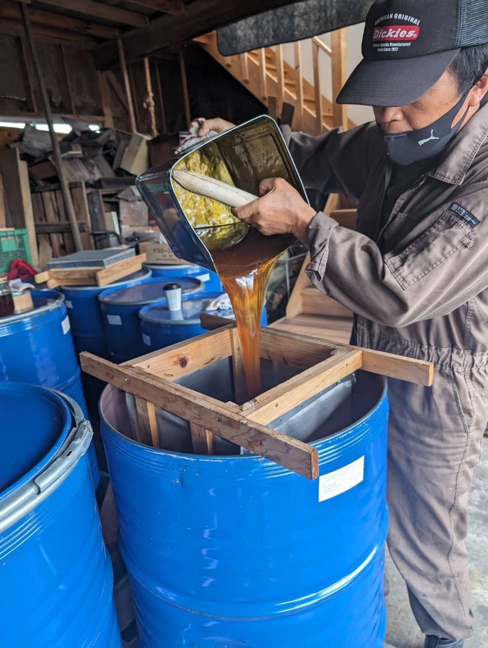 一斗缶にいれたはちみつをドラム缶にうつしているところ