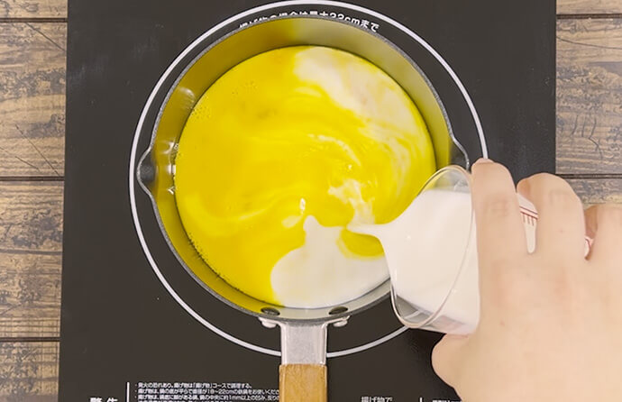 卵を溶き、鍋に入れて牛乳とハンガリー産アカシアはちみつを加える様子